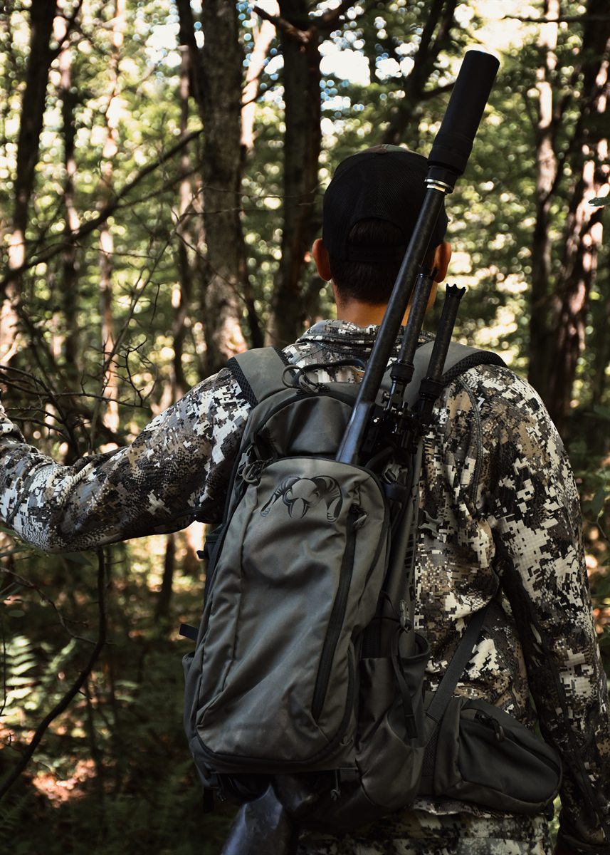 Hunter walking into the woods with a Peregrine-equipped rifle slung on a pack