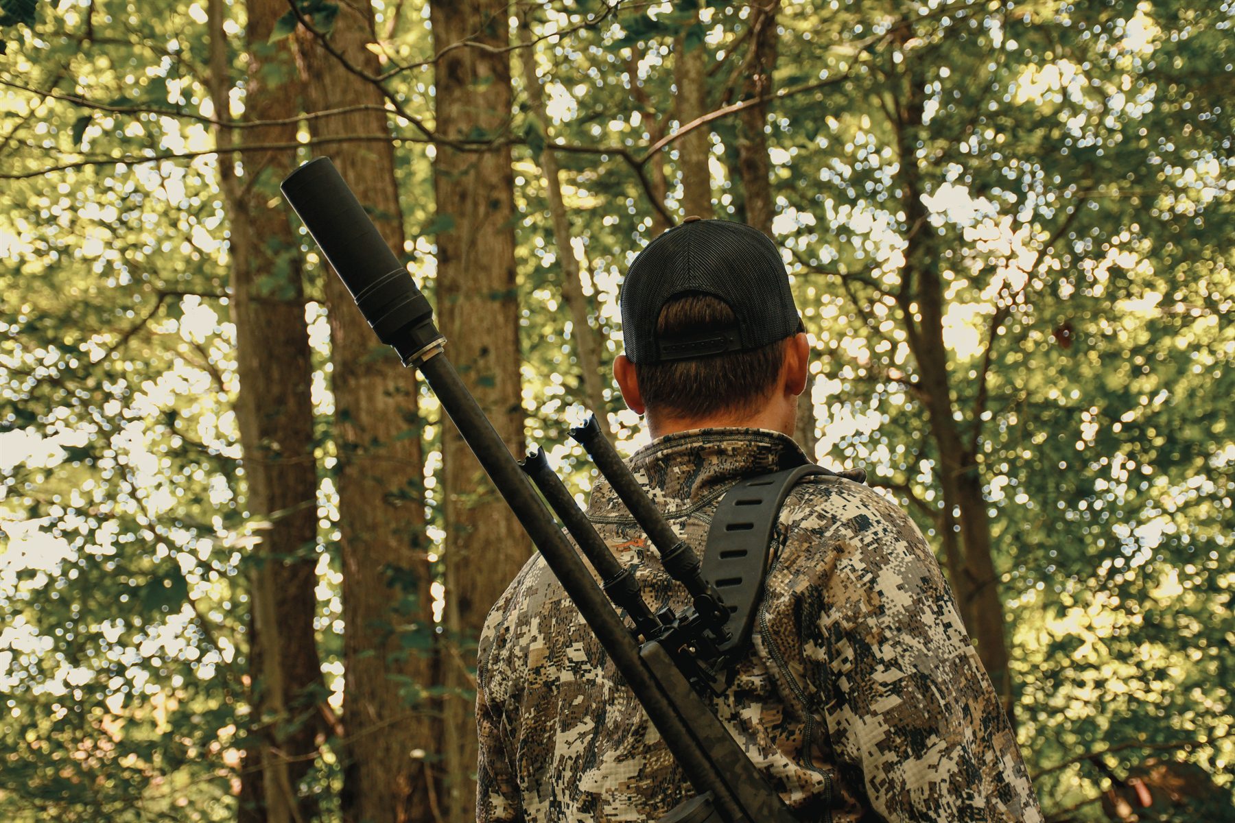 Hunter in camo moving through the timber, suppressed rifle over the shoulder