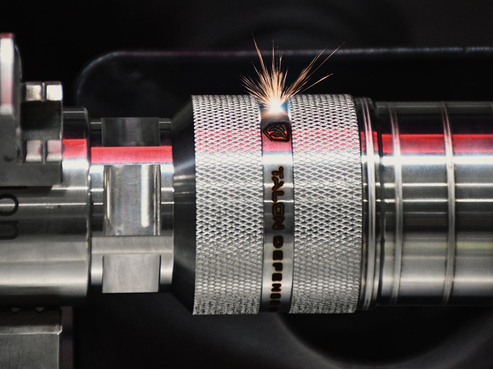 Laser engraving the Talon shield onto a knurled suppressor body, spark plume rising from the beam